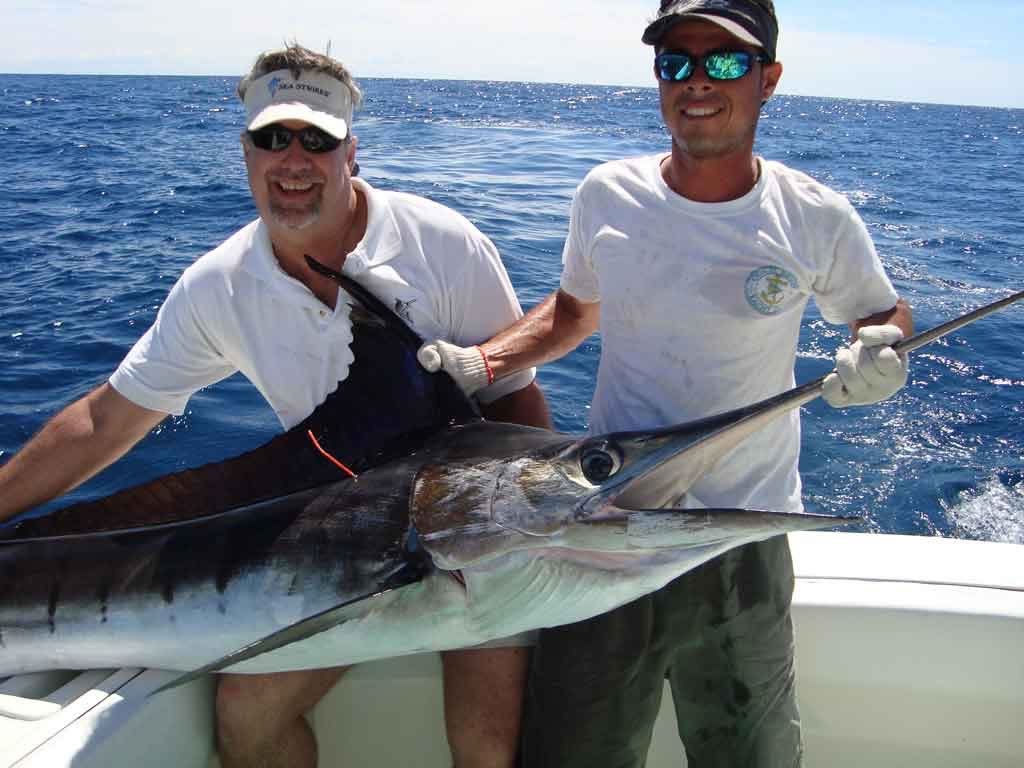 Bruce and a mate holding a marlin boatside in blue water